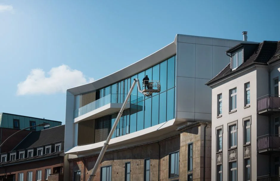 A worker cleaning skyscraper windows with a harness in an urban setting.